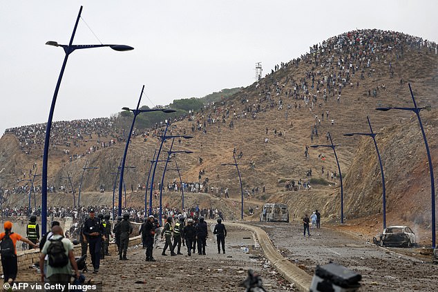 Moroccan security forces watch thousands of migrants on a hillside at the border with Spain